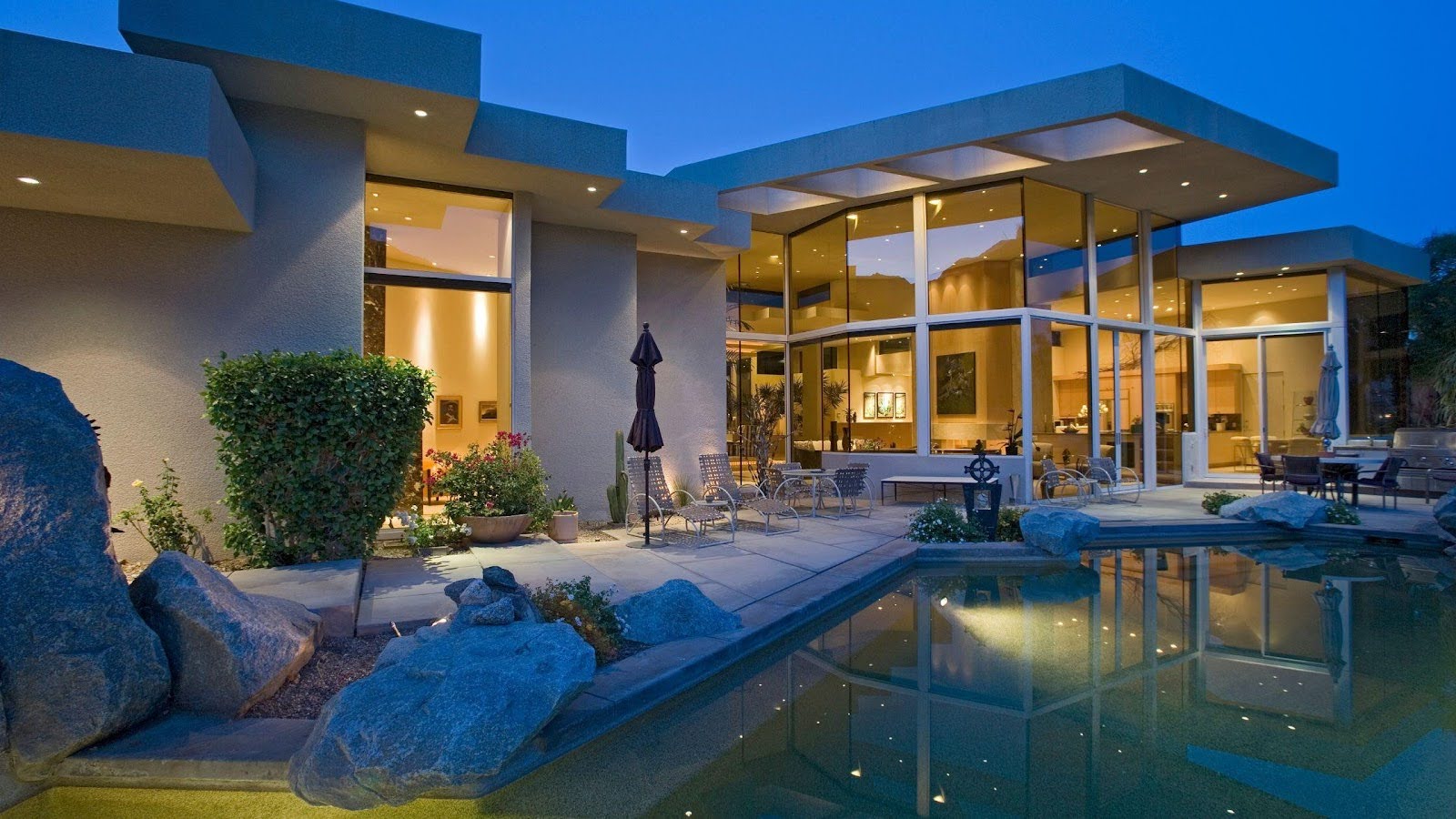 A luxurious modern home with expansive glass walls and sleek architectural lines, illuminated in the evening. 